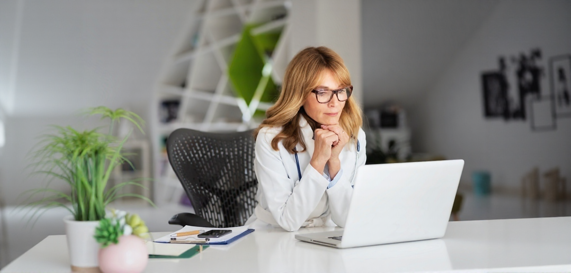 A physician sits at her desk and focuses on her laptop screen.