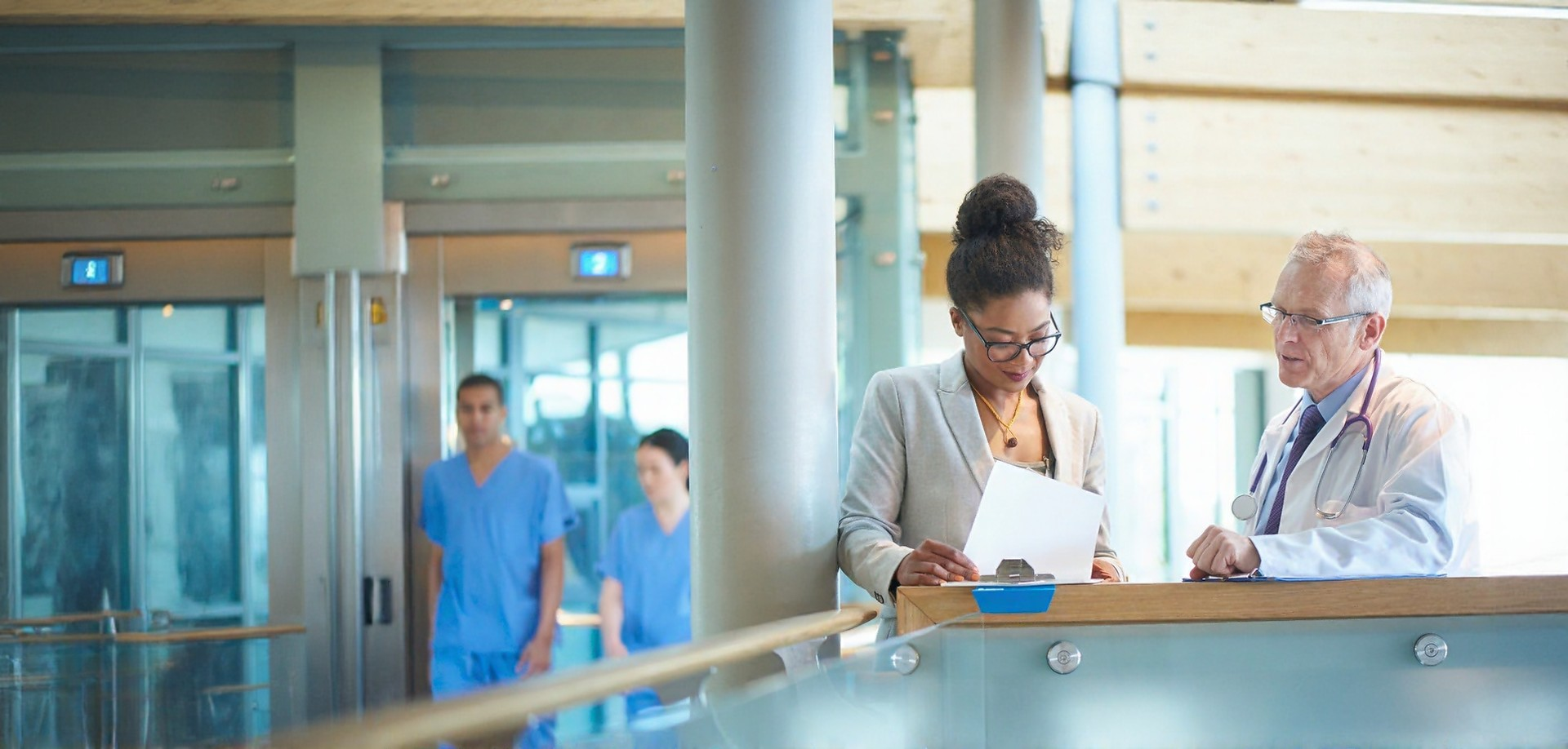 A physician and an administrator review patient data in a hospital hallway.